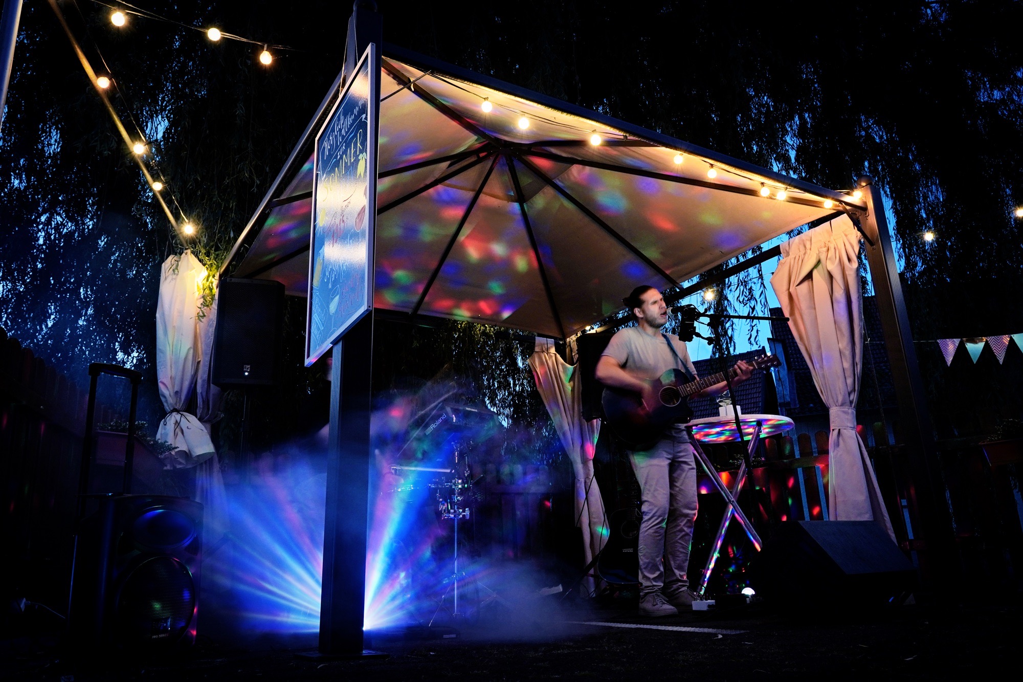 Liveband spielt auf Sommerfest unter Lichterkette mit Gitarre und Nebel