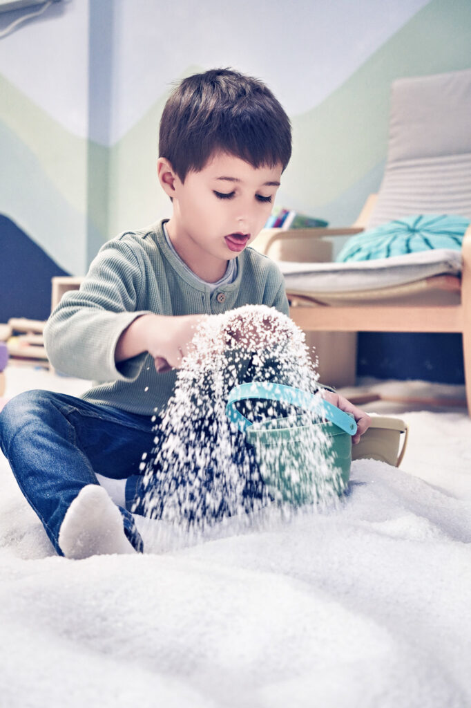 Junge spielt mit Salz und Eimer auf dem Boden des Spielbereichs