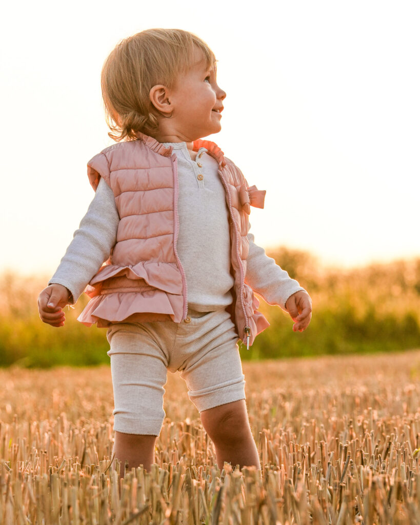 Kleinkind im rosa Outfit läuft über ein abgeerntetes Feld bei Sonnenuntergang in Bruchköbel, aufgenommen bei einem natürlichen Familienshooting