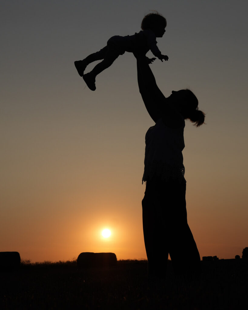 Mutter hebt ihr Kind liebevoll in die Höhe, eingerahmt von der untergehenden Sonne im Main-Kinzig-Kreis