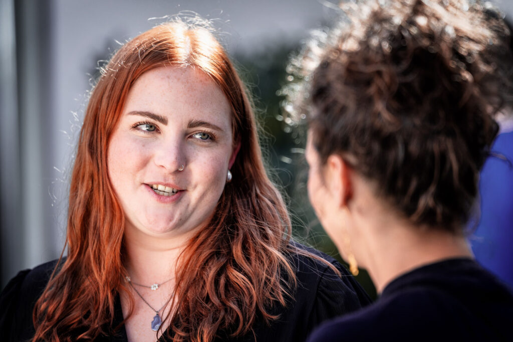 Junge Frau mit roten Haaren im Gespräch bei Geburtstagsfeier im Rhein-Main-Gebiet – natürliche Momentaufnahme.
