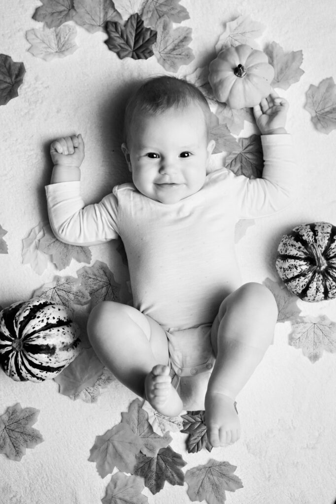 Baby liegt zwischen Blättern und kleinen Kürbissen, Schwarzweiß.