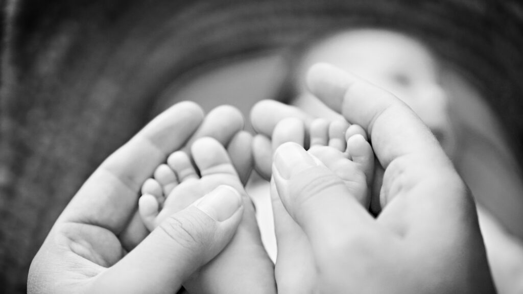 Eltern umschließen zarte Babyfüße in einer schützenden Geste, Schwarzweiß.
