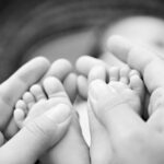 Eltern umschlie&szlig;en zarte Babyf&uuml;&szlig;e in einer sch&uuml;tzenden Geste, Schwarzwei&szlig;.