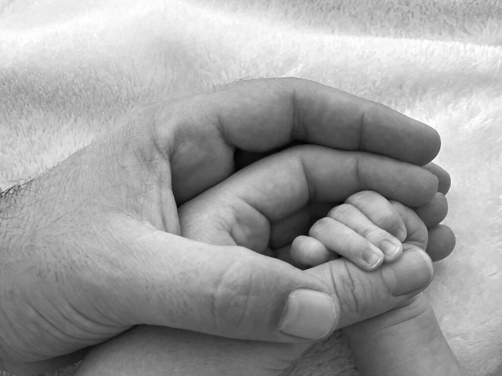 Winzige Babyhand greift den Daumen eines Elternteils, Schwarzweiß.