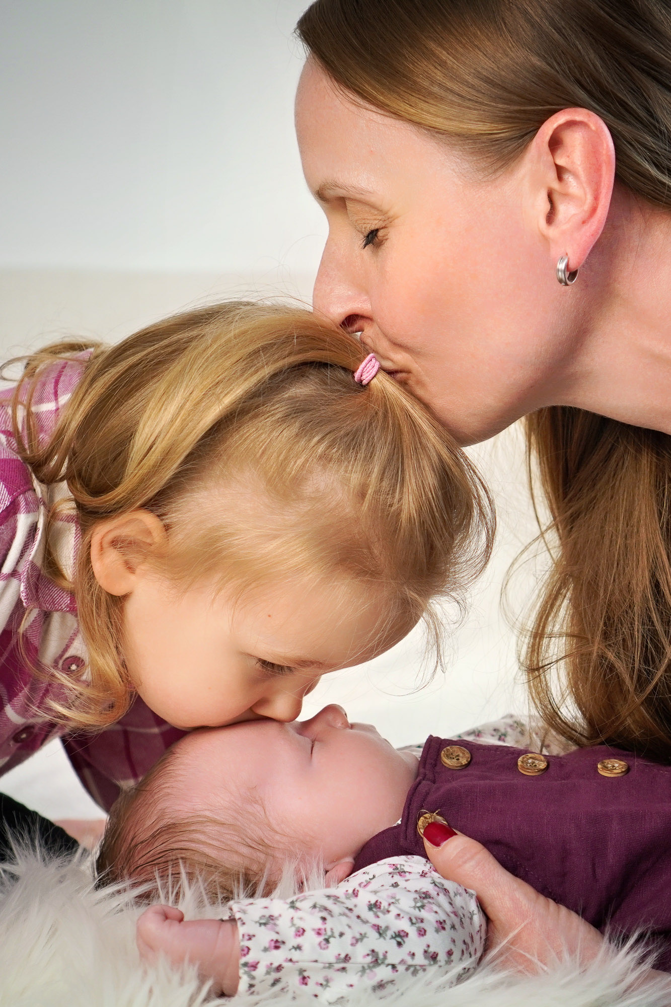 Gro&szlig;e Schwester k&uuml;sst das Baby auf die Stirn &ndash; Familienfoto beim Newbornshooting in Hanau