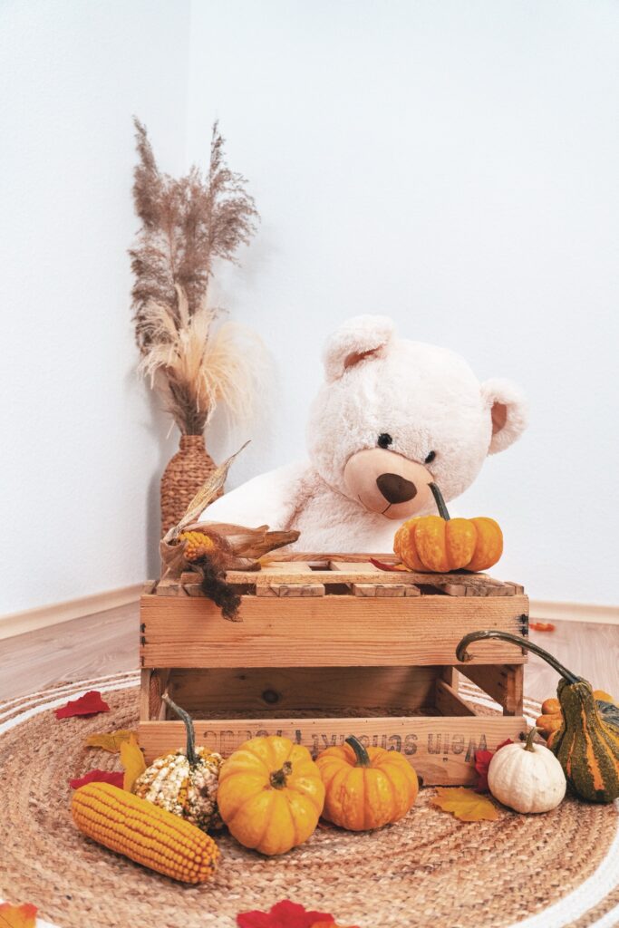 Herbstliche Deko mit B&auml;r, K&uuml;rbissen und Trockenblumen in einer hellen Ecke
