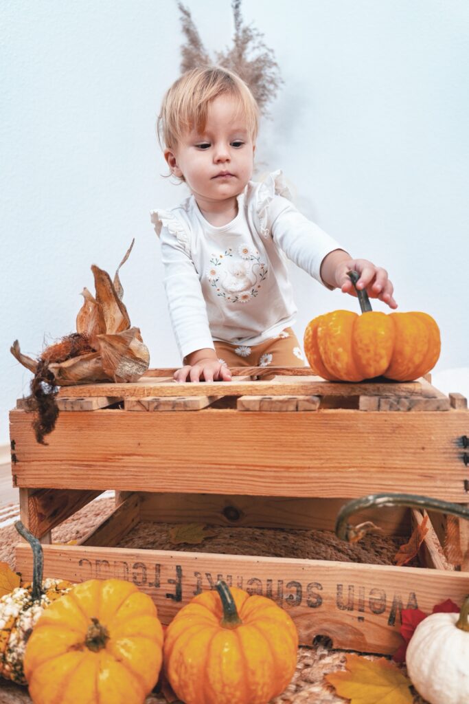 Kleines Kind spielt mit K&uuml;rbis an herbstlicher Holzbox