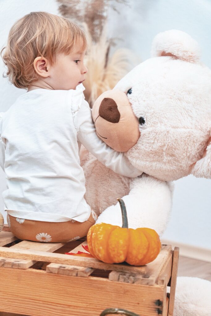 Kleines Kind kuschelt mit gro&szlig;em Pl&uuml;schb&auml;ren neben K&uuml;rbissen