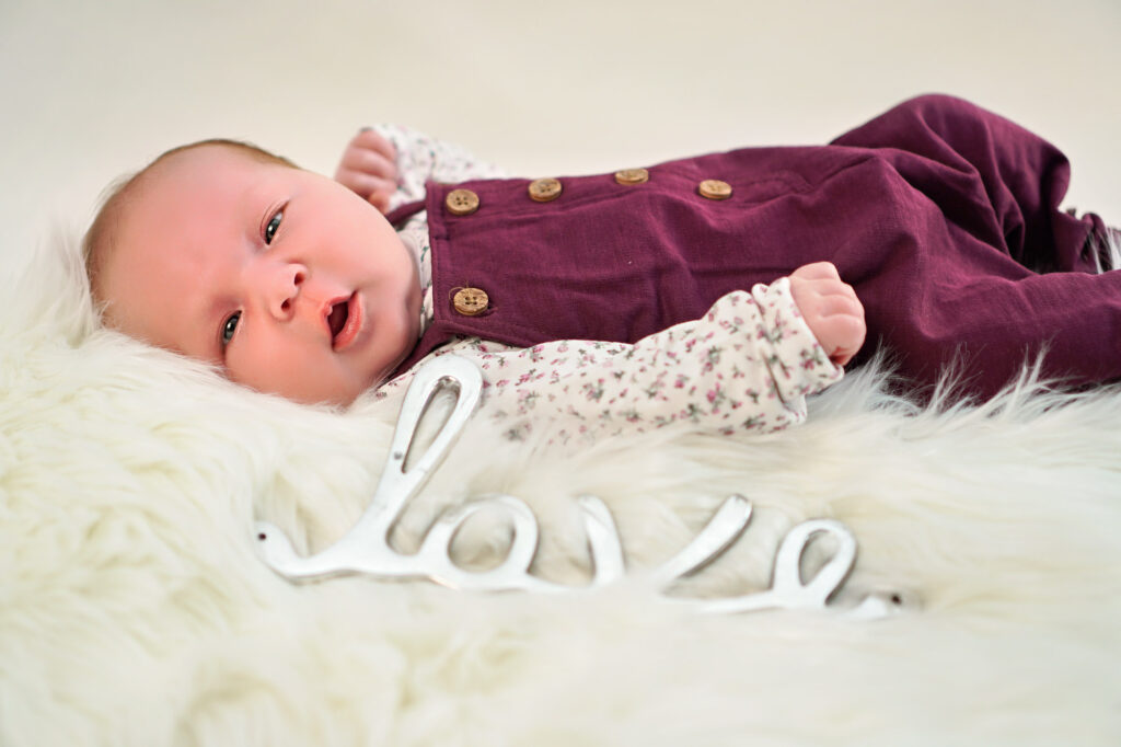 Baby liegt auf wei&szlig;em Fell mit silbernem Love-Schriftzug &ndash; Newborn-Foto in Bruchk&ouml;bel
