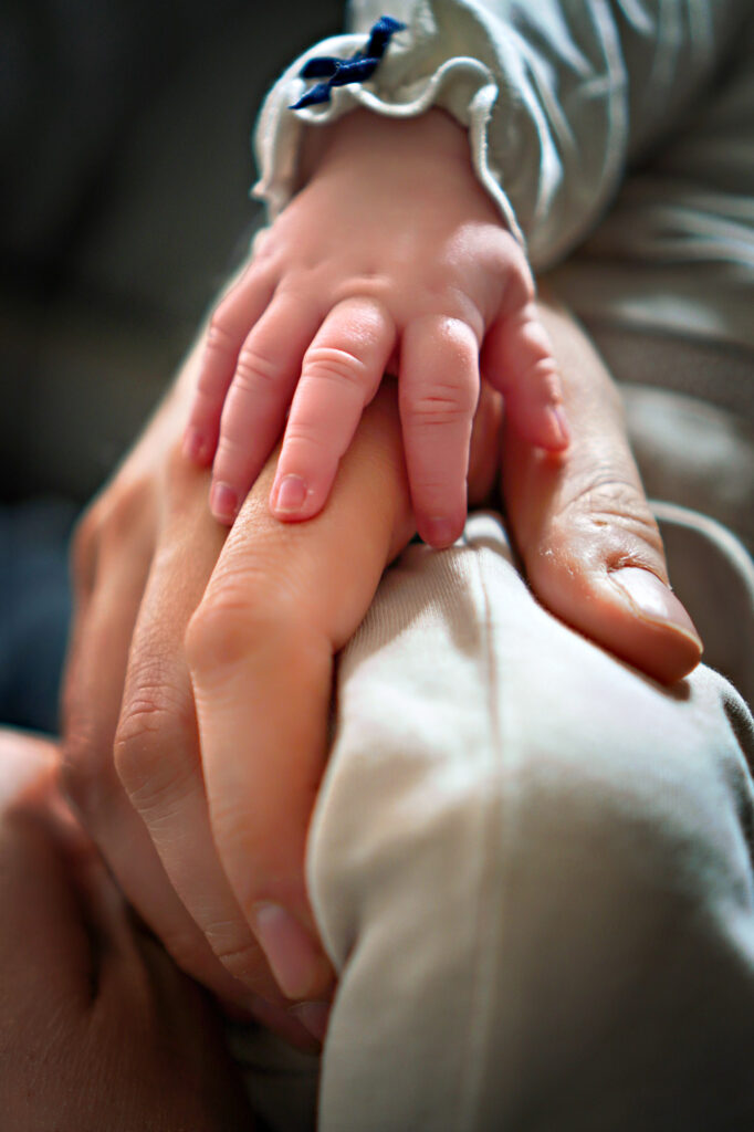 Babyhand liegt sanft auf der Hand eines Elternteils beim Newborn-Shooting