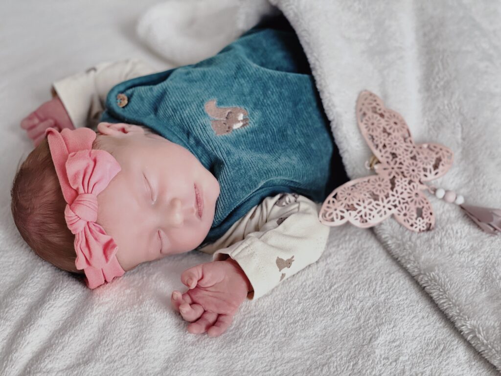 Schlafendes Neugeborenes mit rosa Stirnband und Schmetterlingsdekoration auf weicher Decke