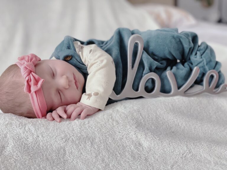 Schlafendes Neugeborenes mit rosa Stirnband und Dekoelement &bdquo;Love&ldquo; auf weicher Decke