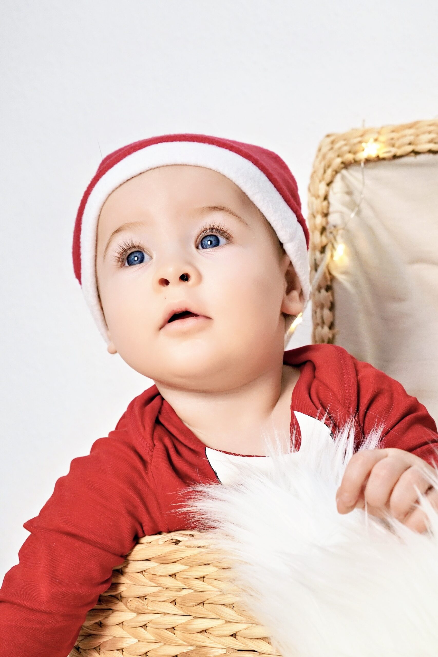 Baby mit roter Nikolausmütze schaut staunend nach oben, im Hintergrund leuchten kleine Lichter