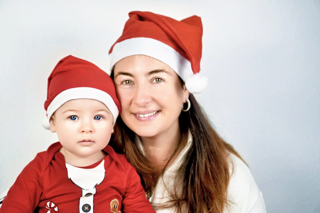 Mutter und Baby tragen Nikolausmützen und lächeln gemeinsam in die Kamera