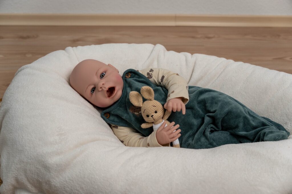 Babypuppe liegt auf dem Boden im Nest chen mit Kuscheltier in der Hand