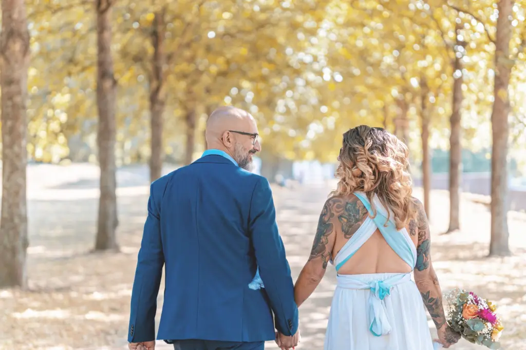 Brautpaar spaziert Arm in Arm durch eine herbstliche Allee