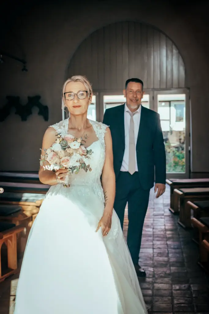 Braut mit Brautstrau&szlig; im Vordergrund, dahinter der Br&auml;utigam, in der dunklen Kapelle mit Rundbogen