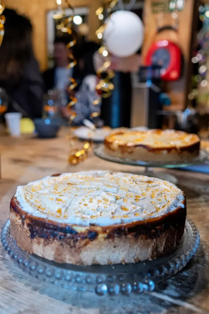 Kuchen mit goldbraun &uuml;berbackener Haube auf einer Glasplatte, dahinter ein zweiter Kuchen am Kuchenbuffet