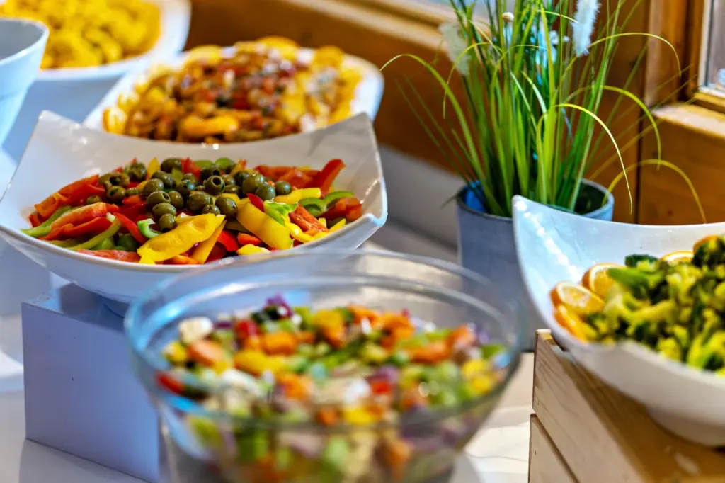Bunt angerichtete Salate und Gem&uuml;se in wei&szlig;en Schalen und einer Glassch&uuml;ssel auf dem Buffet