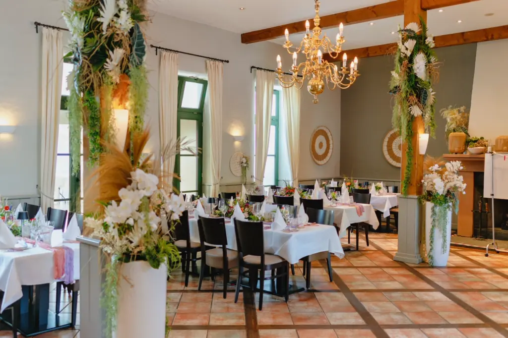 Festsaal mit Kronleuchter, Blumen- und Pflanzenschmuck an den S&auml;ulen und eingedeckten Tischen