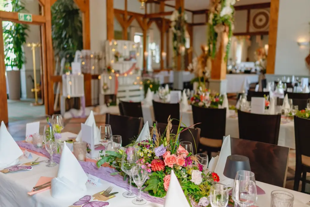 Blumengestecke in Rosa und Lila auf einer langen Festtafel mit Weingl&auml;sern und gefalteten Servietten